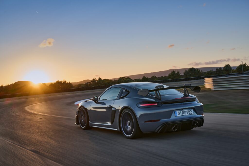 A Porsche 718 Cayman GT4 RS drives on a track and showcases its wing. 