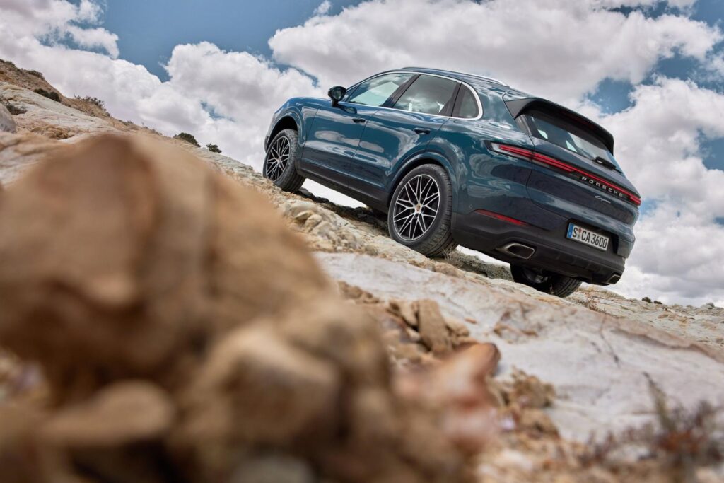 A blue Porsche Cayenne climbs up a rocky path.
